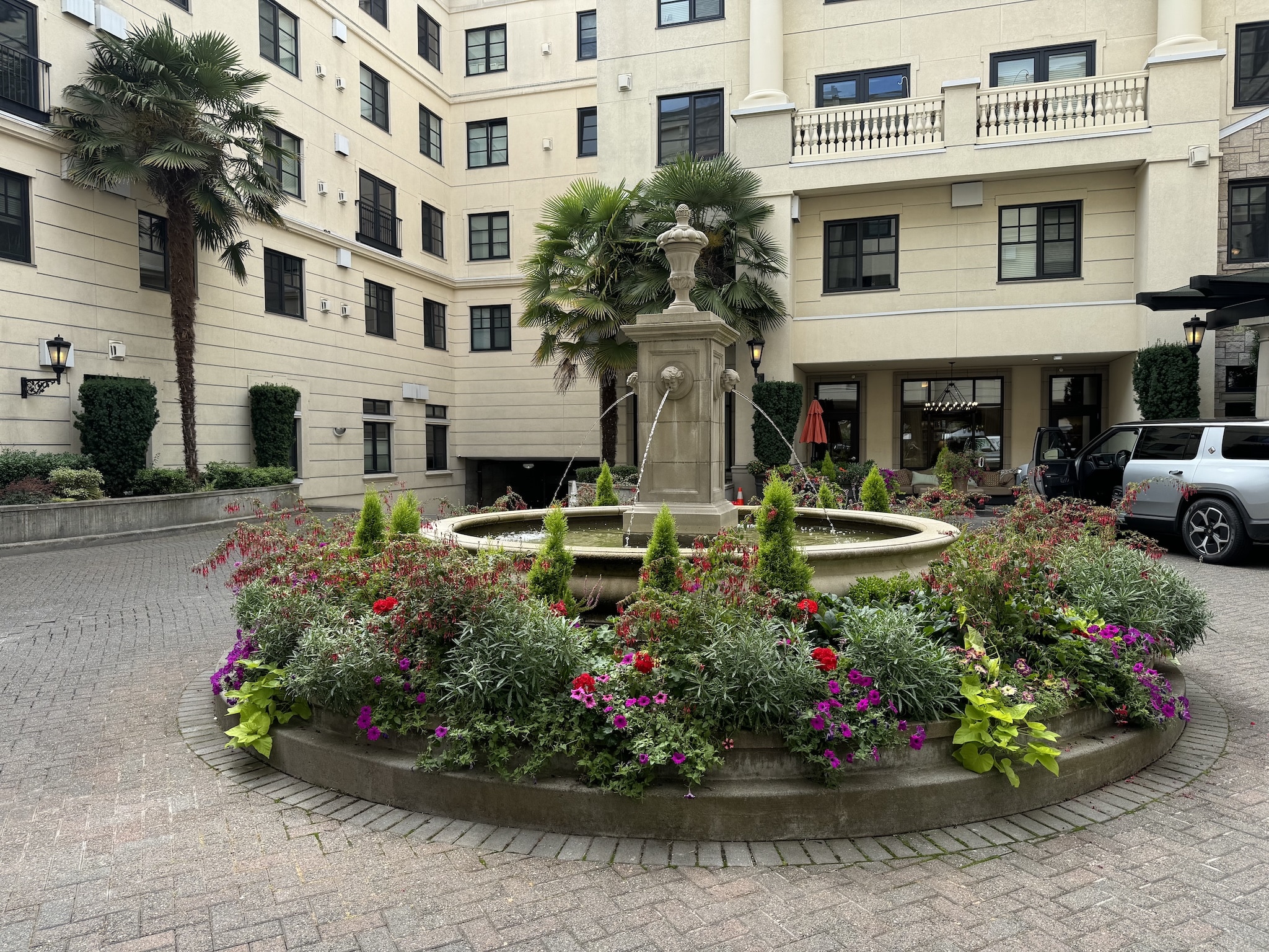 Circular planter around a fountain filled with red, purple, and white seasonal flowers at a building entrance.