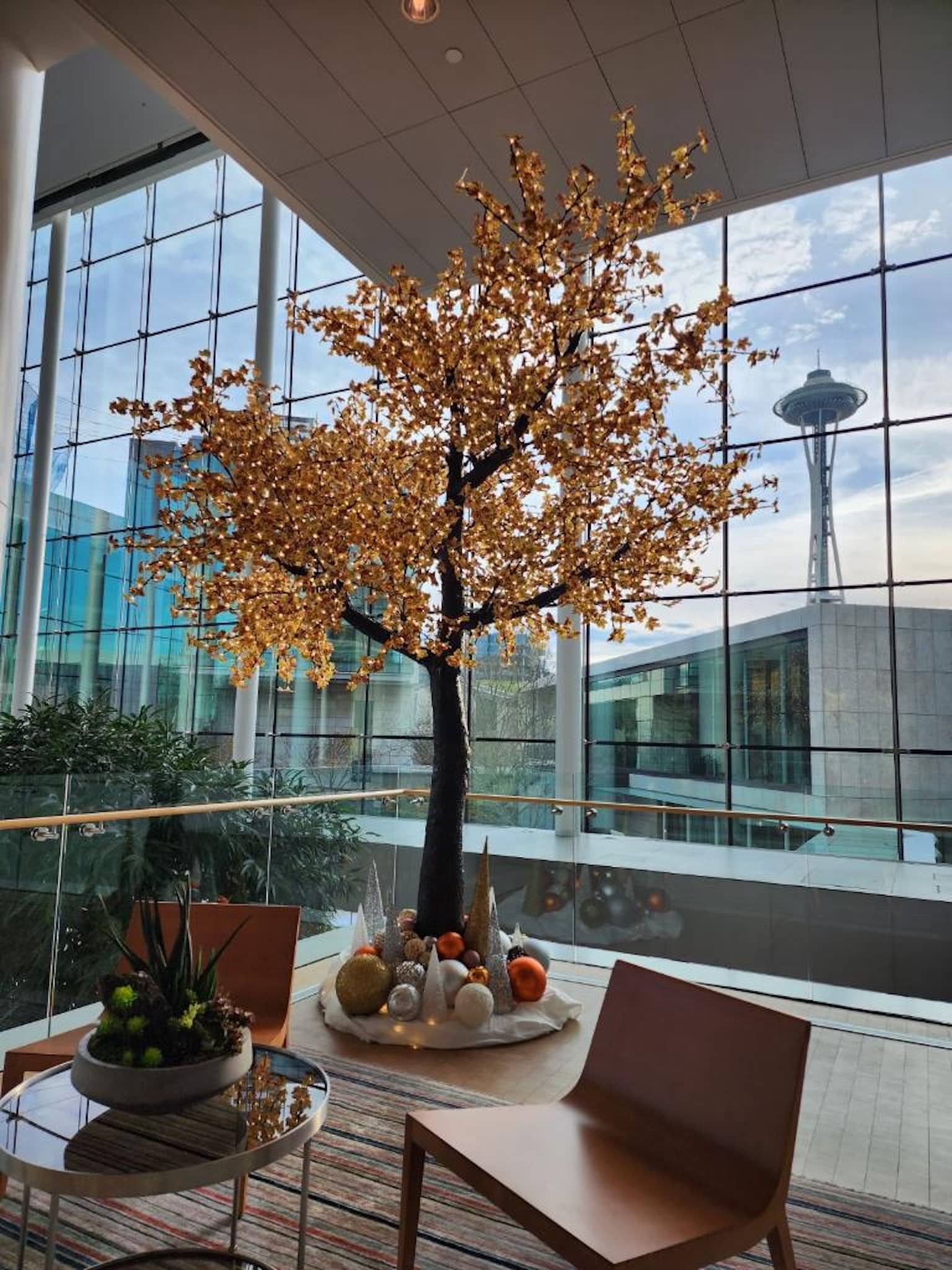 Illuminated decorative tree with Space Needle in background – Golden-lit tree by large windows with Seattle skyline visible