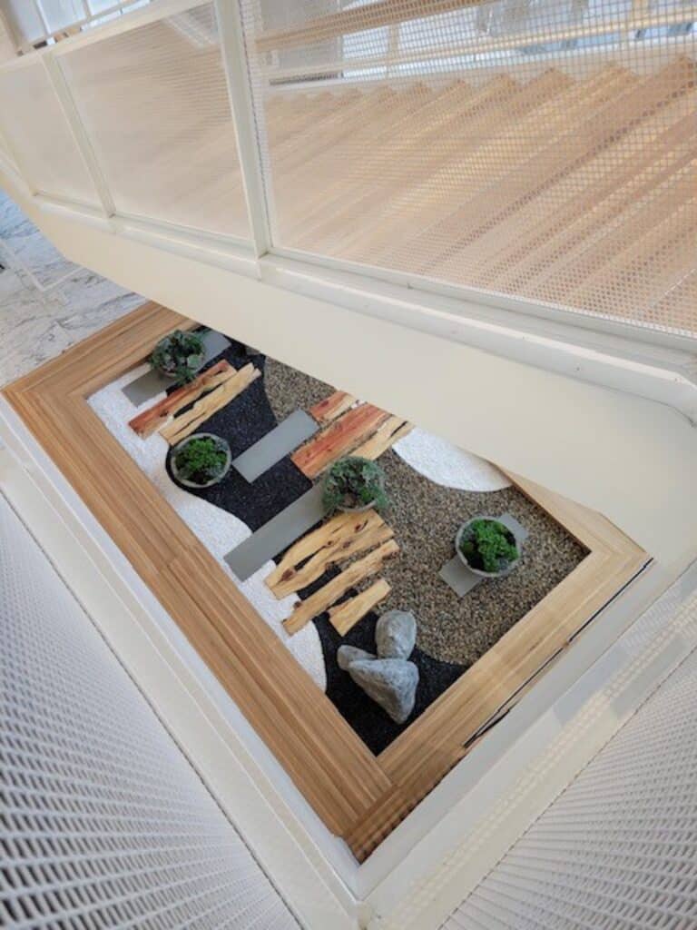 Minimalist Japanese-style indoor zen garden with stone, gravel, and wood textures beneath stairwell.
