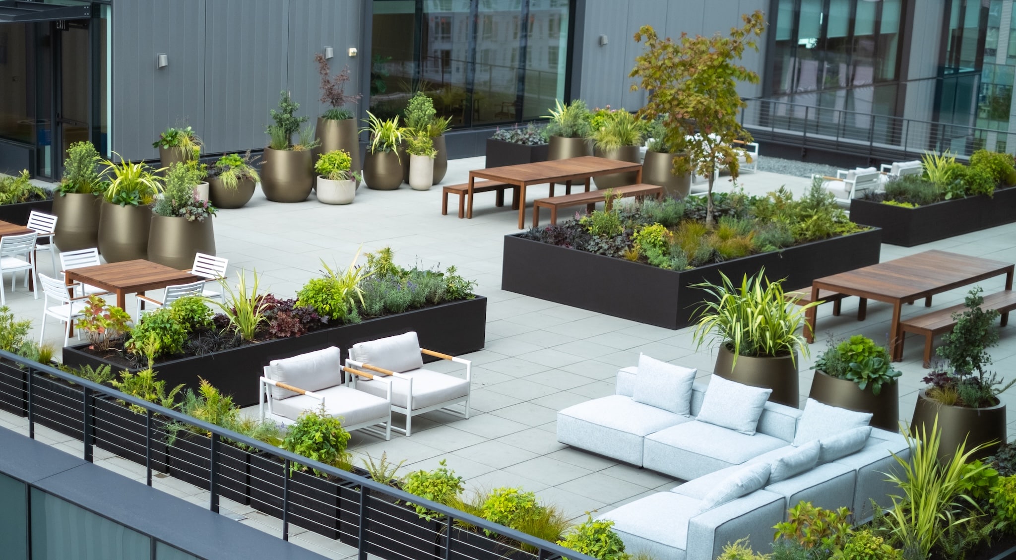 Wide rooftop view showing patterned planter layout with tables and lounging areas.