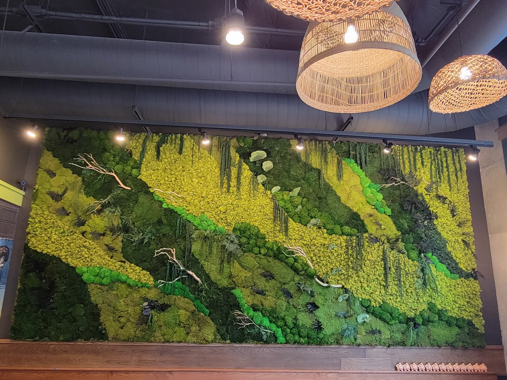 Large-scale moss wall in restaurant with dramatic lighting and layered botanical textures