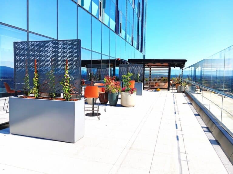 Tall modern planters and geometric privacy screens framing a rooftop seating area with glass railings and skyline views.