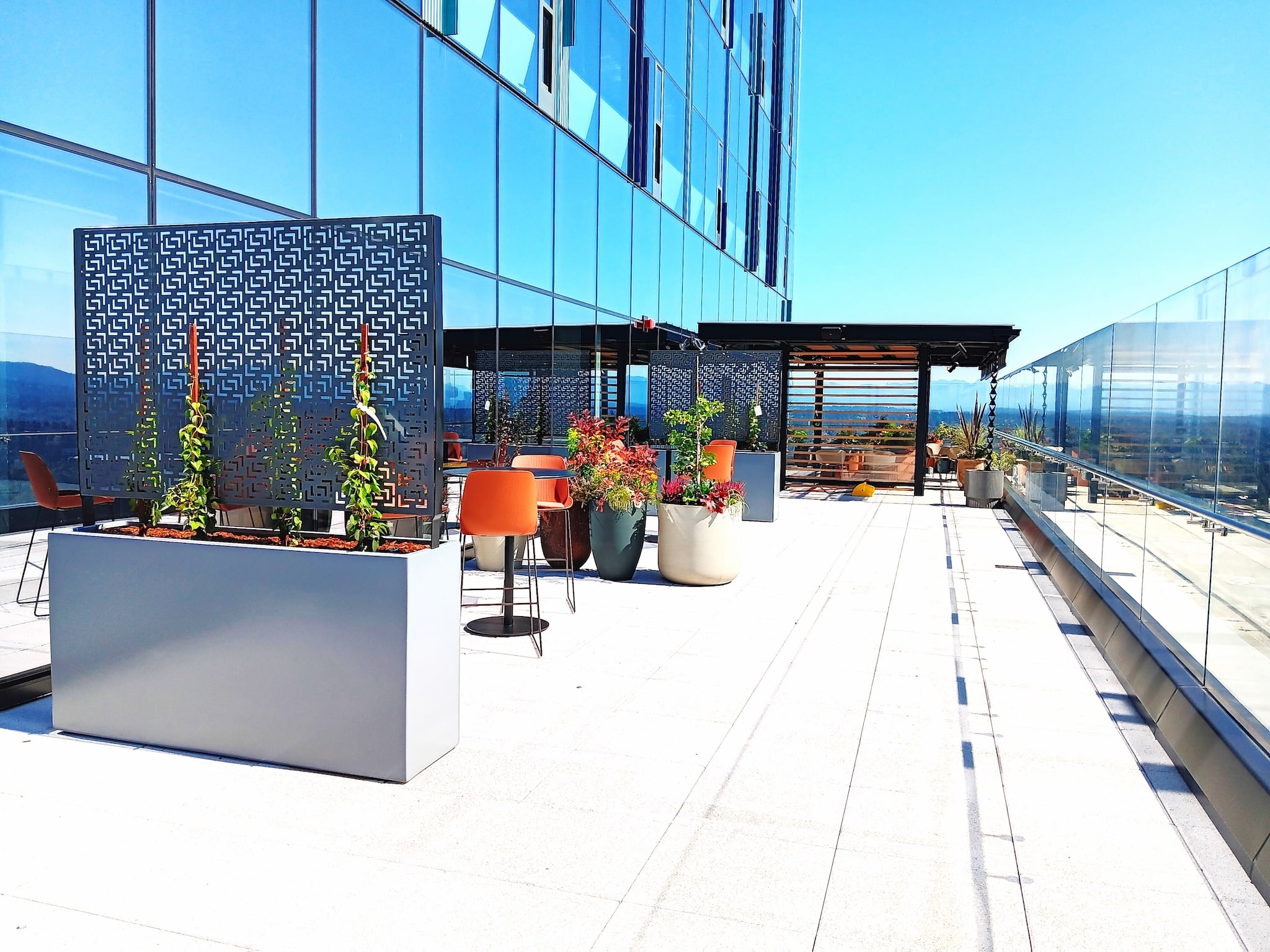Tall modern planters and geometric privacy screens framing a rooftop seating area with glass railings and skyline views.
