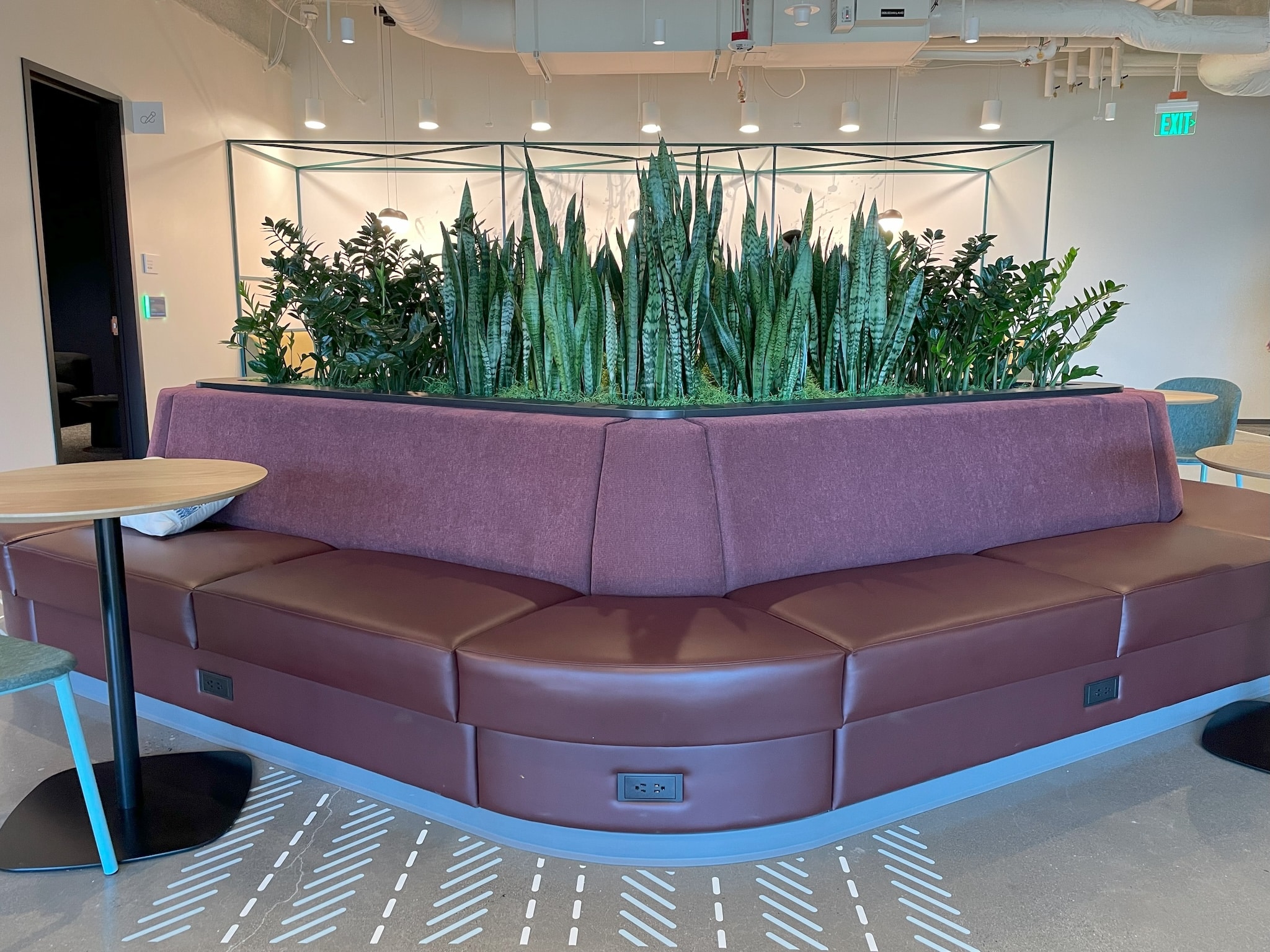 A modern waiting room with circular seating arrangement upholstered in a light color, complemented by a large planter filled with lush greenery in the center, creating a welcoming and comfortable space.