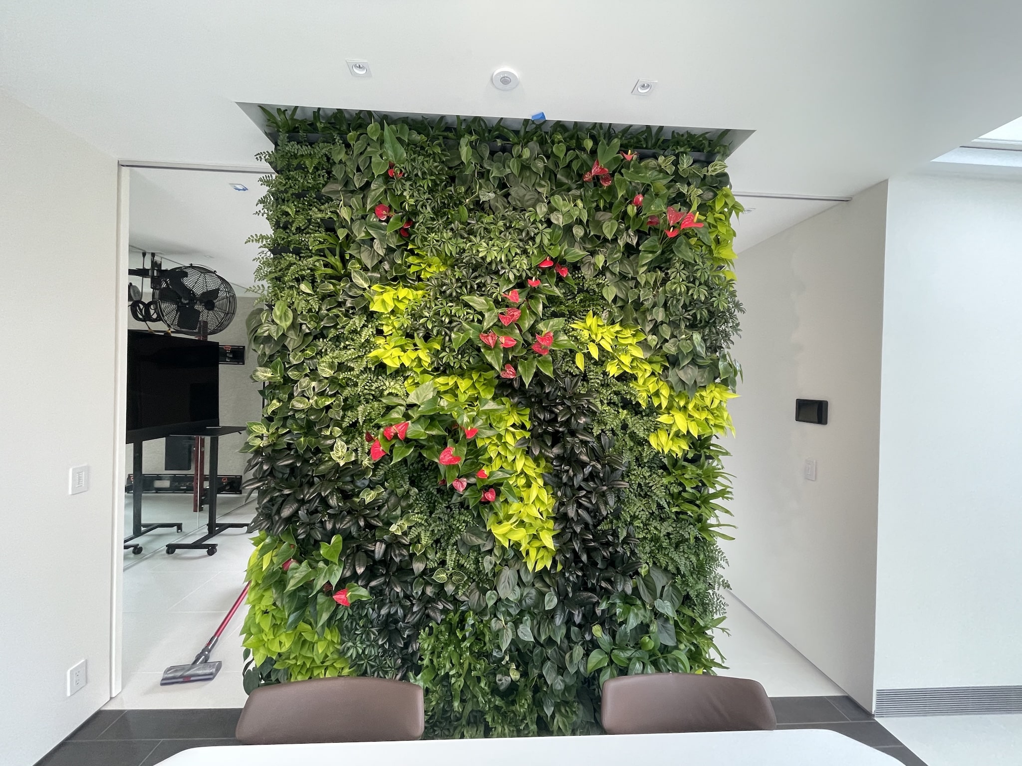 Bright indoor living wall featuring dense tropical foliage with pops of red flowers and lime-green leaves
